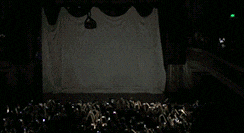 a crowd of people sitting in front of a stage with a white curtain