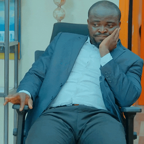 a man in a suit sits in a chair with his hand on his chin