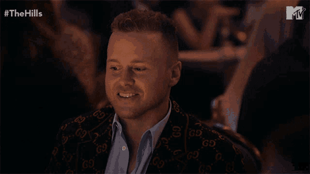 a man wearing a gucci jacket sits at a table in front of a mtv logo