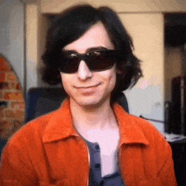 a man wearing sunglasses and an orange jacket is smiling for the camera .