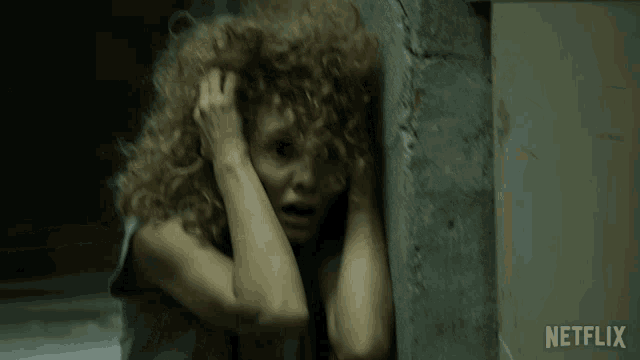 a woman with curly hair is hiding behind a wall with netflix written on the bottom