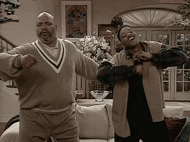 two men are dancing in a living room in front of a couch