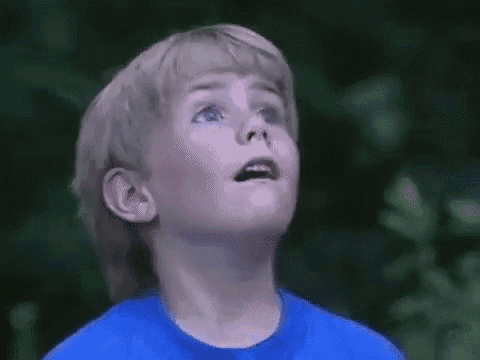 a young boy in a blue shirt is looking up at something in the sky .
