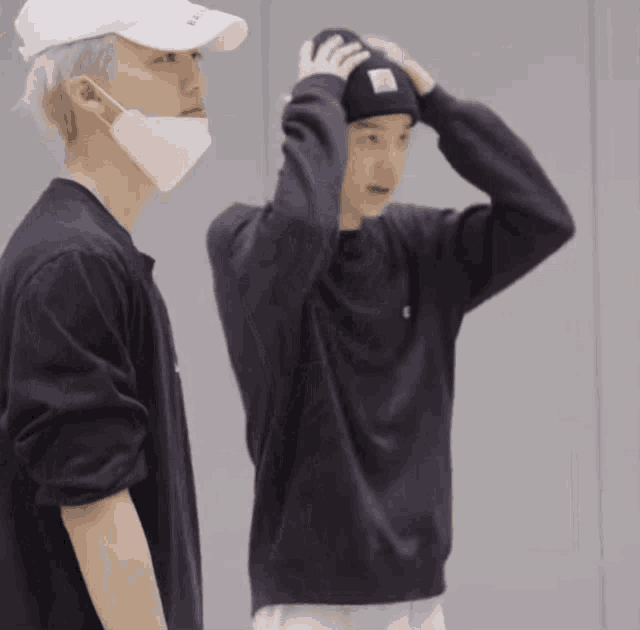 a man wearing a mask and a white hat is standing next to another man wearing a black sweater