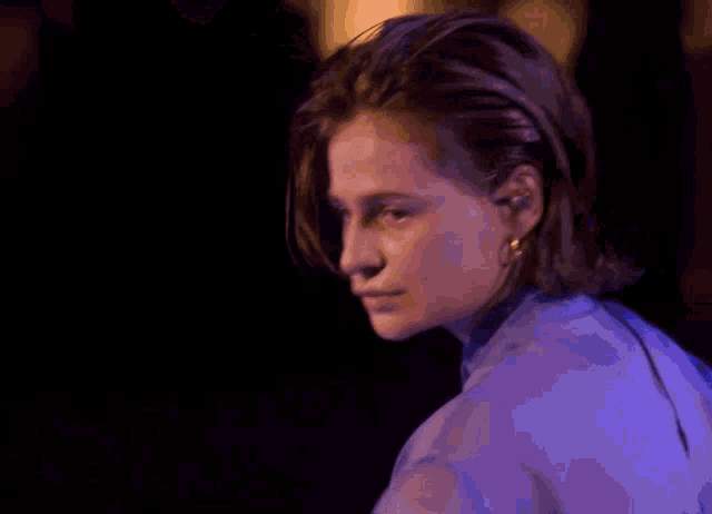 a woman in a purple shirt is smiling in a dark room with a blue light behind her .