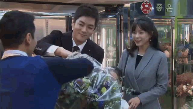 a man in a suit is holding a bouquet of flowers in front of a woman
