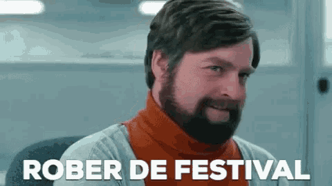 a man with a beard is sitting in a chair with the words rober de festival written on the screen behind him .