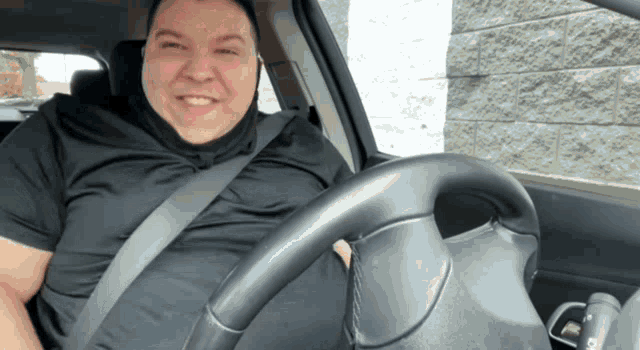 a man wearing a black shirt and a seat belt is driving a car