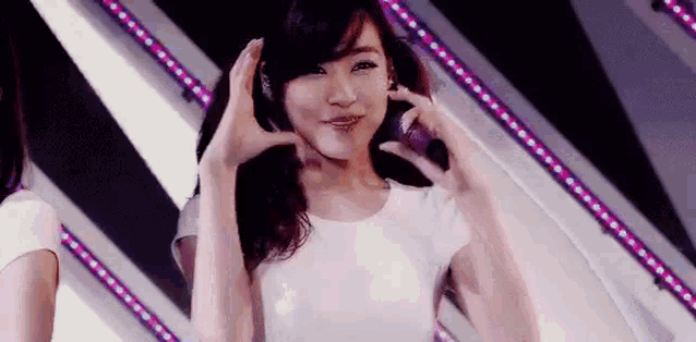 a young woman in a white shirt is making a heart shape with her hands .