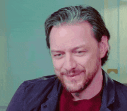 a man with gray hair and a beard is smiling and wearing a blue jacket .