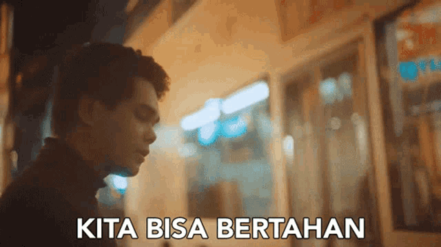 a man stands in front of a building with the words kita bisa bertahan below him