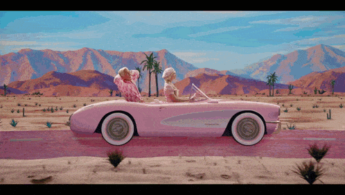 two women are riding in a pink corvette in the desert