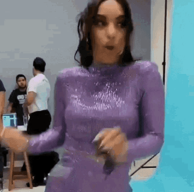 a woman in a purple dress is dancing in front of a blue wall .