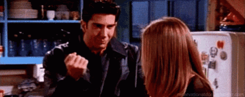 a man and a woman are standing next to each other in a kitchen and the man is making a fist .