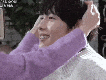 a person in a purple sweater is touching a man 's head