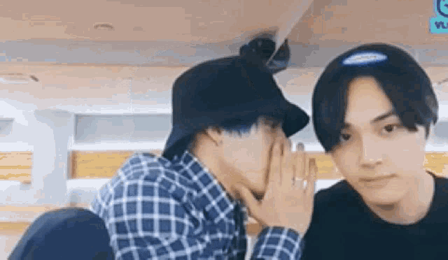 a man is whispering something into another man 's ear while wearing a hat .