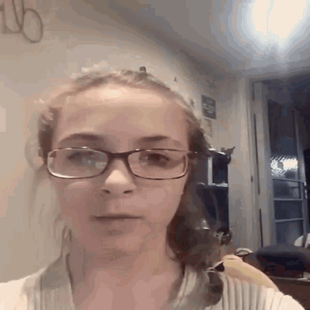 a girl wearing glasses looks at the camera in a room