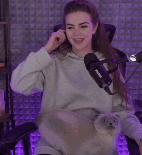 a woman sitting in front of a shure microphone and a cat