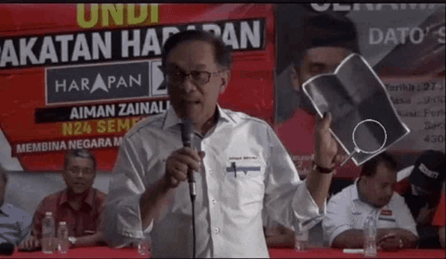 a man speaking into a microphone in front of a banner that says ' harapan ' on it