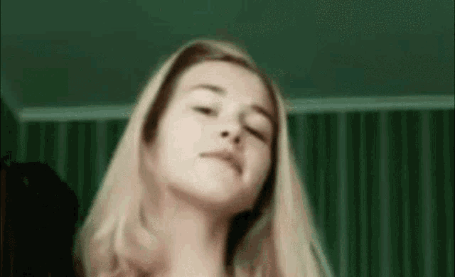 a close up of a woman 's face with her eyes closed in a room with green curtains .