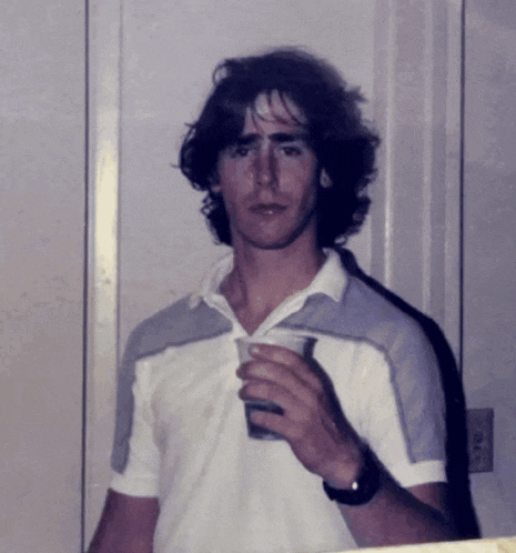 a man in a white shirt is holding a glass