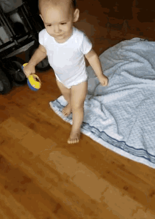 a baby in a white bodysuit is standing on a wooden floor
