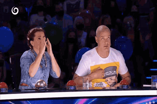 a man wearing a t-shirt with a picture of a man on it sits next to a woman who is covering her face