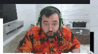 a man with a beard wearing headphones and a hawaiian shirt is sitting in a living room .