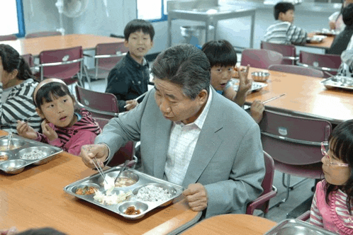 a man in a suit is holding a tray of food in front of a group of children