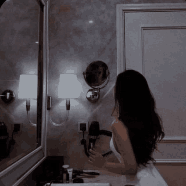 a woman is standing in a bathroom looking at herself in the mirror .