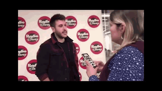 a man is being interviewed by a woman in front of a wall that says radio disney on it