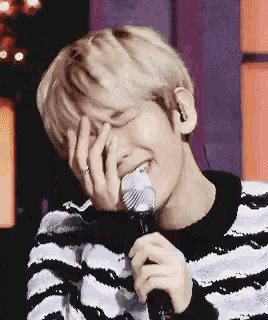 a man in a striped sweater is holding a microphone and covering his face .