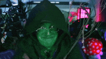 a person with green paint on their face is wearing glasses and a hoodie