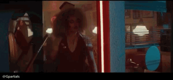 a woman with curly hair is standing in a dark room with a red light behind her .