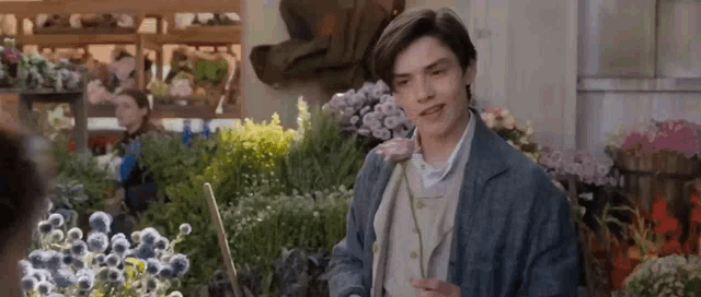 a young man is standing in front of a bunch of flowers in a flower shop .