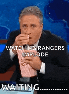 a man in a suit is eating popcorn and watching rangers implode while waiting .