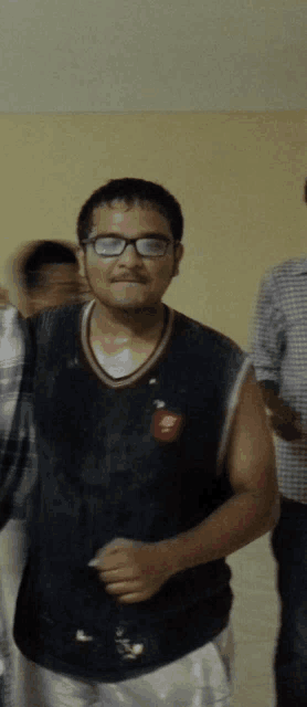 a man wearing glasses and a black tank top has a red emblem on his chest