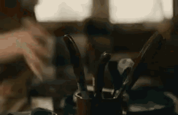 a person is sitting at a table with a bucket of knives and spoons on it .
