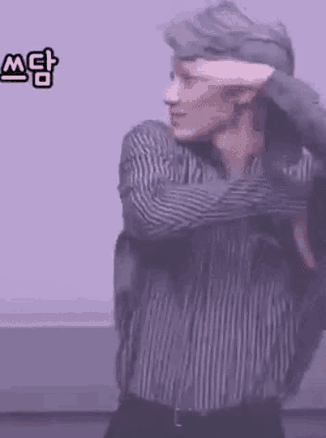 a man in a striped shirt is standing in front of a purple wall .