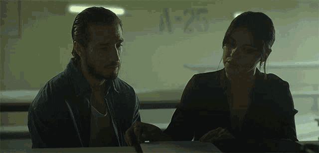 a man and a woman sit at a table in front of a wall that says a-25 on it