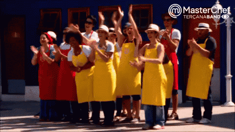 a group of people wearing yellow aprons are clapping in front of a blue building that says master chef