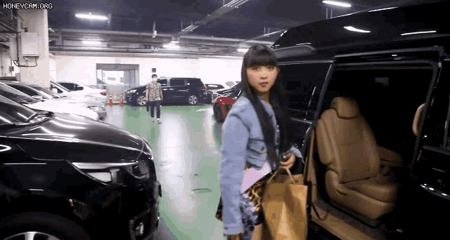 a girl is getting out of a car in a parking garage with the url honeycam.org