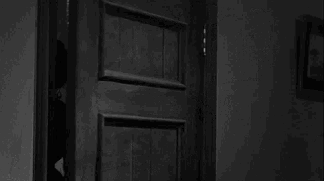 a black and white photo of a woman standing in a doorway holding a cup