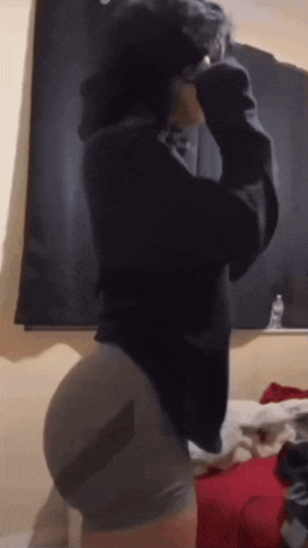 a woman in a black hoodie and shorts is standing in front of a window .