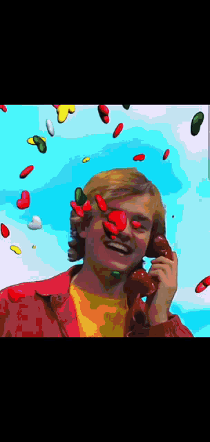 a man is talking on a red phone with jelly beans falling on his face
