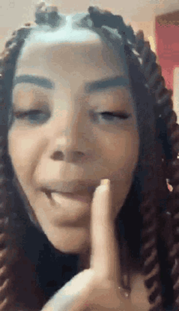 a woman with dreadlocks is making a funny face with her finger to her mouth .