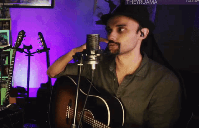 a man singing into a microphone while holding a guitar in front of a sign that says theyruama