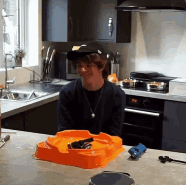 a man wearing a hat is sitting in a kitchen with a toy on the counter