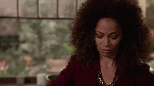 a woman with curly hair is sitting in front of a window with her eyes closed .