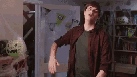 a man in a plaid shirt and a green shirt is dancing in a room with halloween decorations .